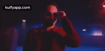 a man in a red jacket and sunglasses is adjusting his sunglasses in a dark room .