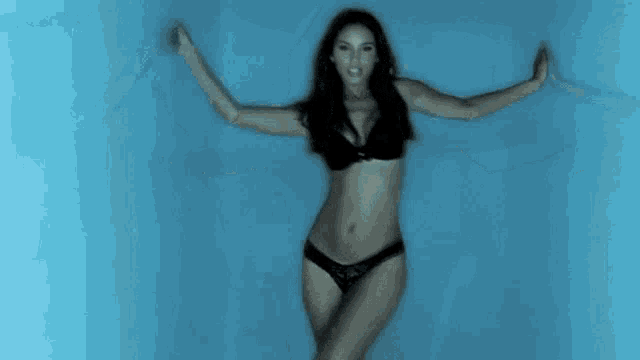 a woman in a black bra and panties is dancing in front of a blue background