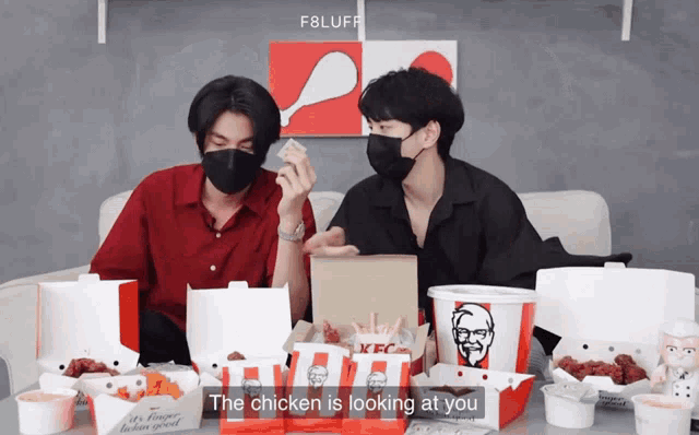two men wearing masks are sitting at a table with boxes of kfc chicken