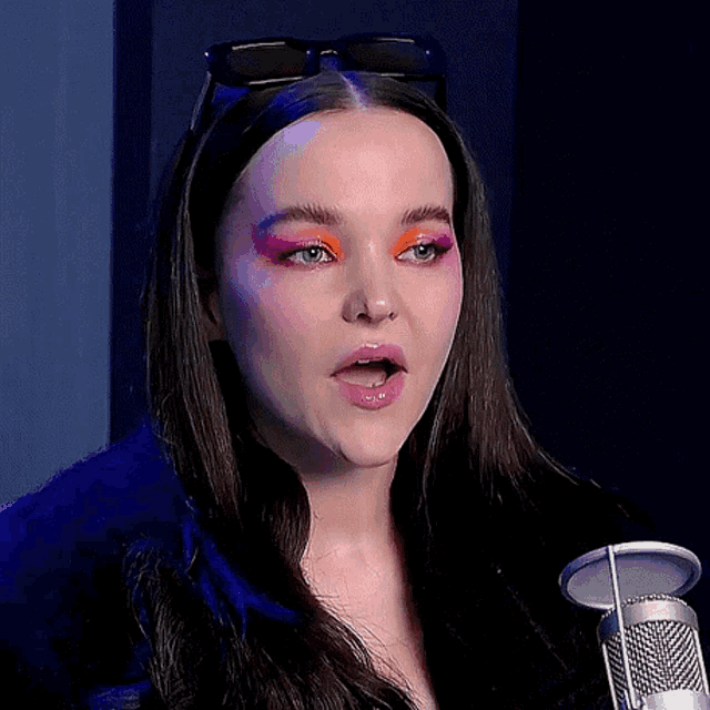 a woman with sunglasses on her head stands in front of a microphone with a surprised look on her face