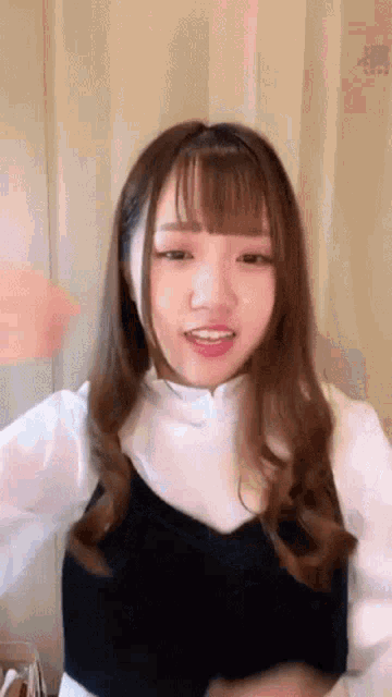a girl with long brown hair and bangs is wearing a white shirt and a black tank top .