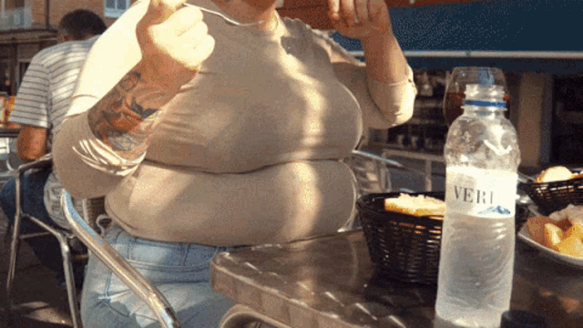 a woman sits at a table with a bottle of vero water next to her