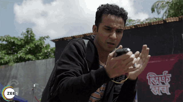 a man is holding a cell phone in front of a sign that says zee5