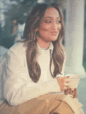 a woman in a white shirt is holding a cup of coffee and smiling