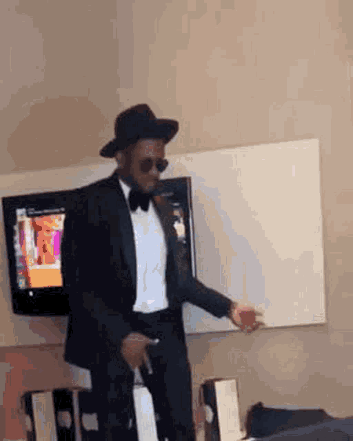 a man in a tuxedo and hat is dancing in a room in front of a television .
