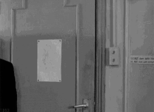 a black and white photo of a man opening a door .