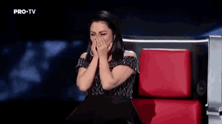 a woman is sitting in a chair with her hands over her mouth .