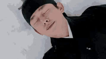 a man in a black hat is laying on the ground with his eyes closed