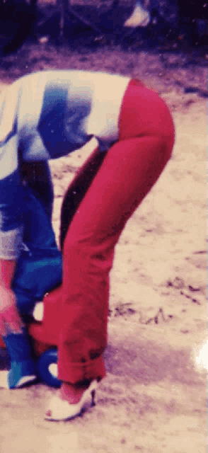 a woman wearing red pants and white heels is kneeling down