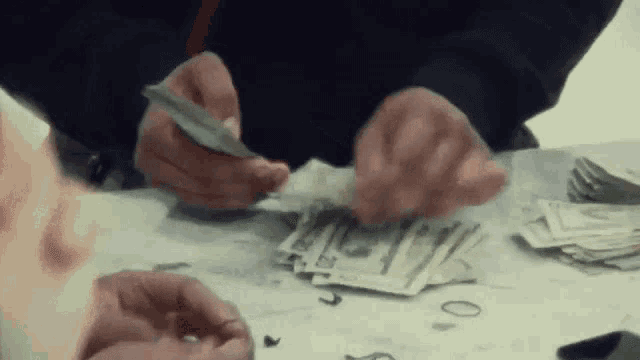 a man is counting money at a table with a pile of money .