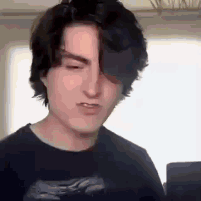 a young man with black hair is making a funny face while looking at a laptop .