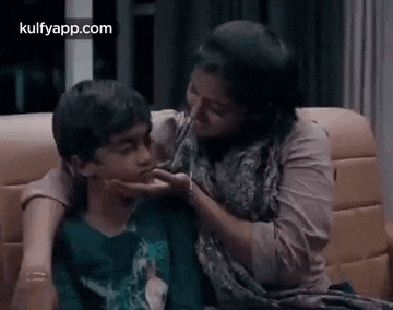a woman is kissing a young boy on the cheek while they are sitting on a couch .