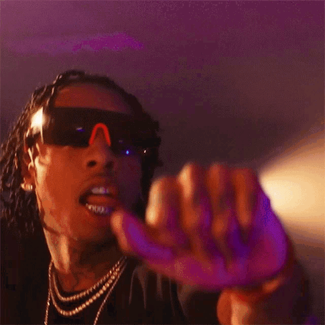 a young man wearing sunglasses and a necklace is making a funny face