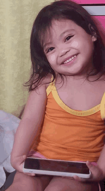 a little girl is smiling while holding a cellphone