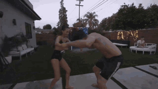 a man and a woman are wrestling in a backyard in front of a house