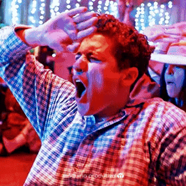 a man in a plaid shirt is screaming with his hands over his head