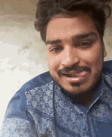 a man with a beard and mustache is sticking his tongue out while wearing a blue shirt .