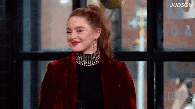 a woman wearing a red velvet jacket and a black top is smiling