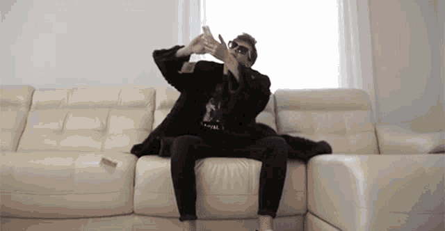 a man wearing sunglasses is sitting on a couch with his hands in the air