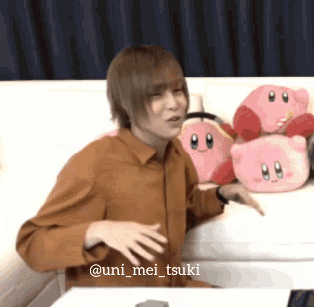 a man sitting on a couch with stuffed animals and the name uni_mei_tsuki on the bottom right