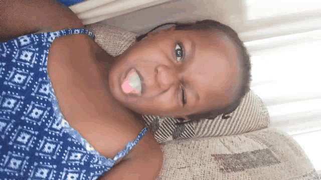 a young girl laying on a couch with her tongue out