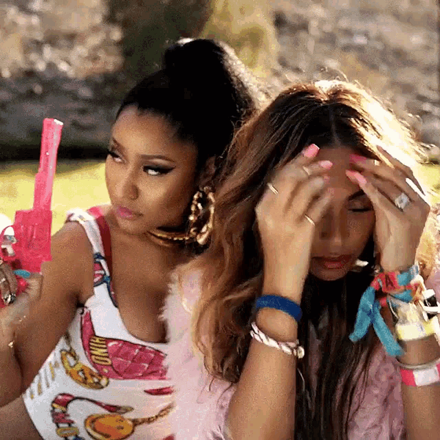 a woman holding a pink toy gun next to another woman who is holding her head