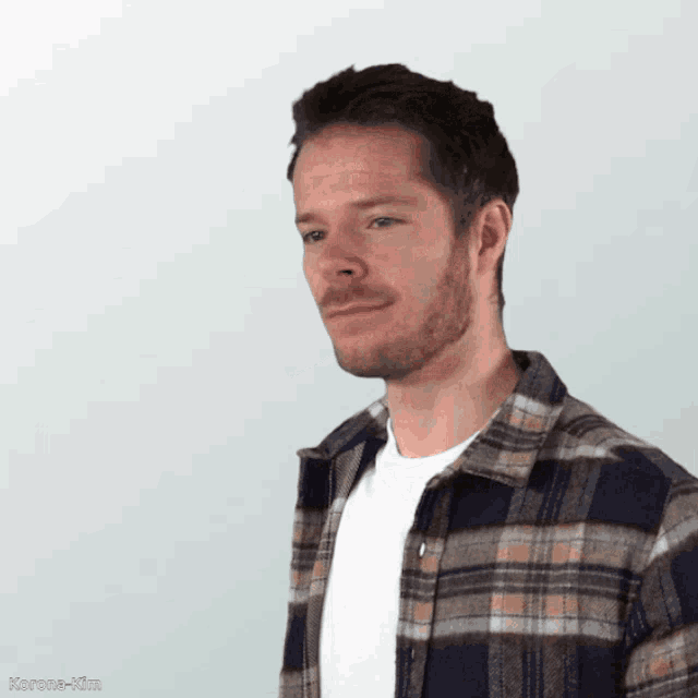 a man wearing a plaid shirt and a white t-shirt looks to his left
