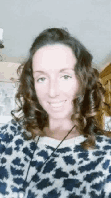 a woman with curly hair is wearing a leopard print sweater and smiling for the camera .