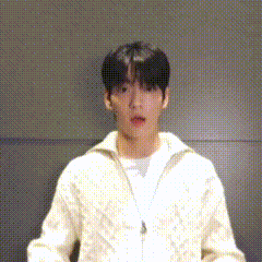 a young man wearing a white sweater is standing in front of a wall .