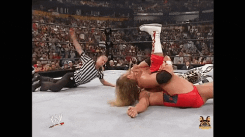 two wrestlers are wrestling in a ring with a referee in the background