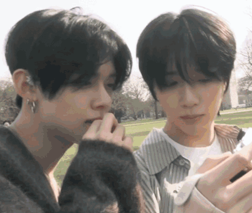 two young men are looking at a cell phone in a park