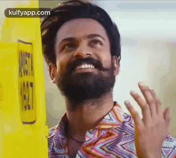 a man with a beard and mustache is smiling and waving while wearing a colorful shirt .