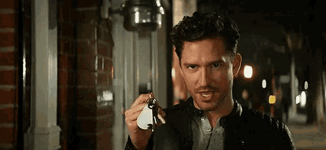 a man in a black jacket is holding a pair of keys in his hand .
