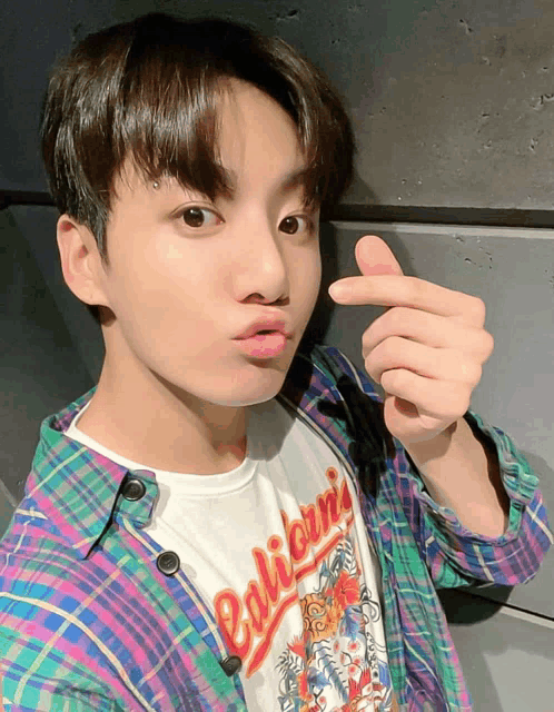 a young man wearing a plaid shirt that says california makes a heart shape with his fingers