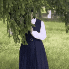 a woman in a blue dress stands in the grass behind a tree