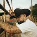 a man with a beard wearing a cowboy hat and a white shirt is standing in front of a fence .