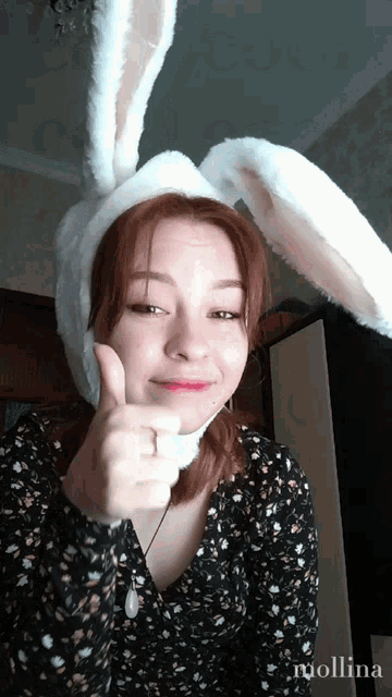 a woman wearing bunny ears gives a thumbs up sign