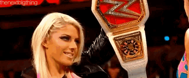 a blonde woman is holding a wrestling championship belt in front of a crowd .