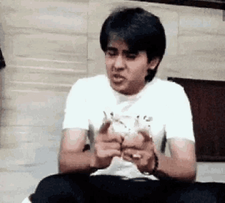 a man in a white t-shirt is sitting on the floor with his hands folded