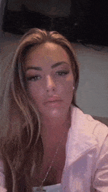 a woman with long blonde hair is wearing a pink jacket and necklace .