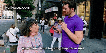 a man in a purple shirt is talking to an elderly woman on a street .