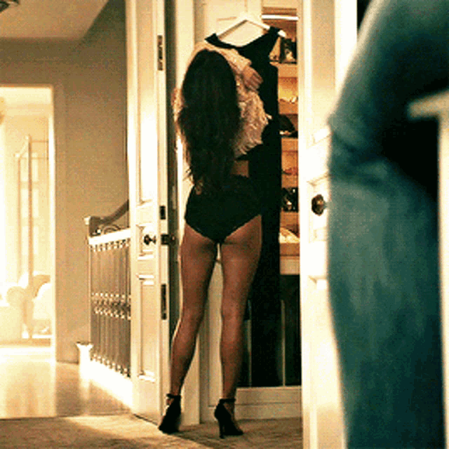 a woman in black underwear is standing in a doorway holding a dress