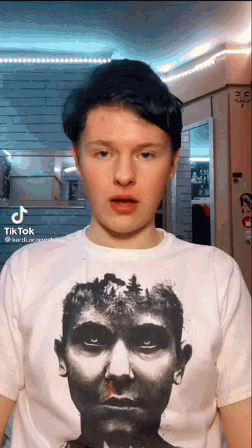 a young man wearing a t-shirt with a picture of a man 's face on it is making a face .