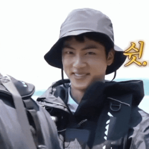 a man wearing a hat and a jacket is smiling while holding a backpack .