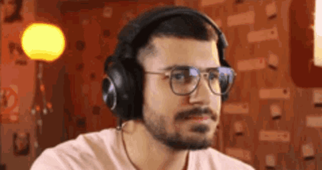 a man with a beard and glasses is wearing headphones and looking at the camera .