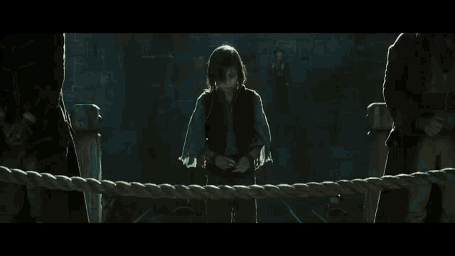 a young girl is standing in a dark room with a man in the background