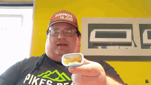 a man wearing a hat that says robbie 's vlog is holding something