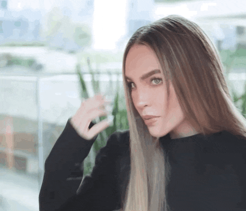 a woman with long hair is wearing a black sweater and looking at the camera .