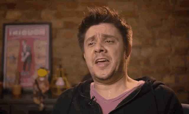 a man is sitting in front of a brick wall making a funny face .