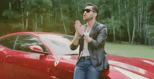 a man wearing sunglasses is standing next to a red ferrari car .